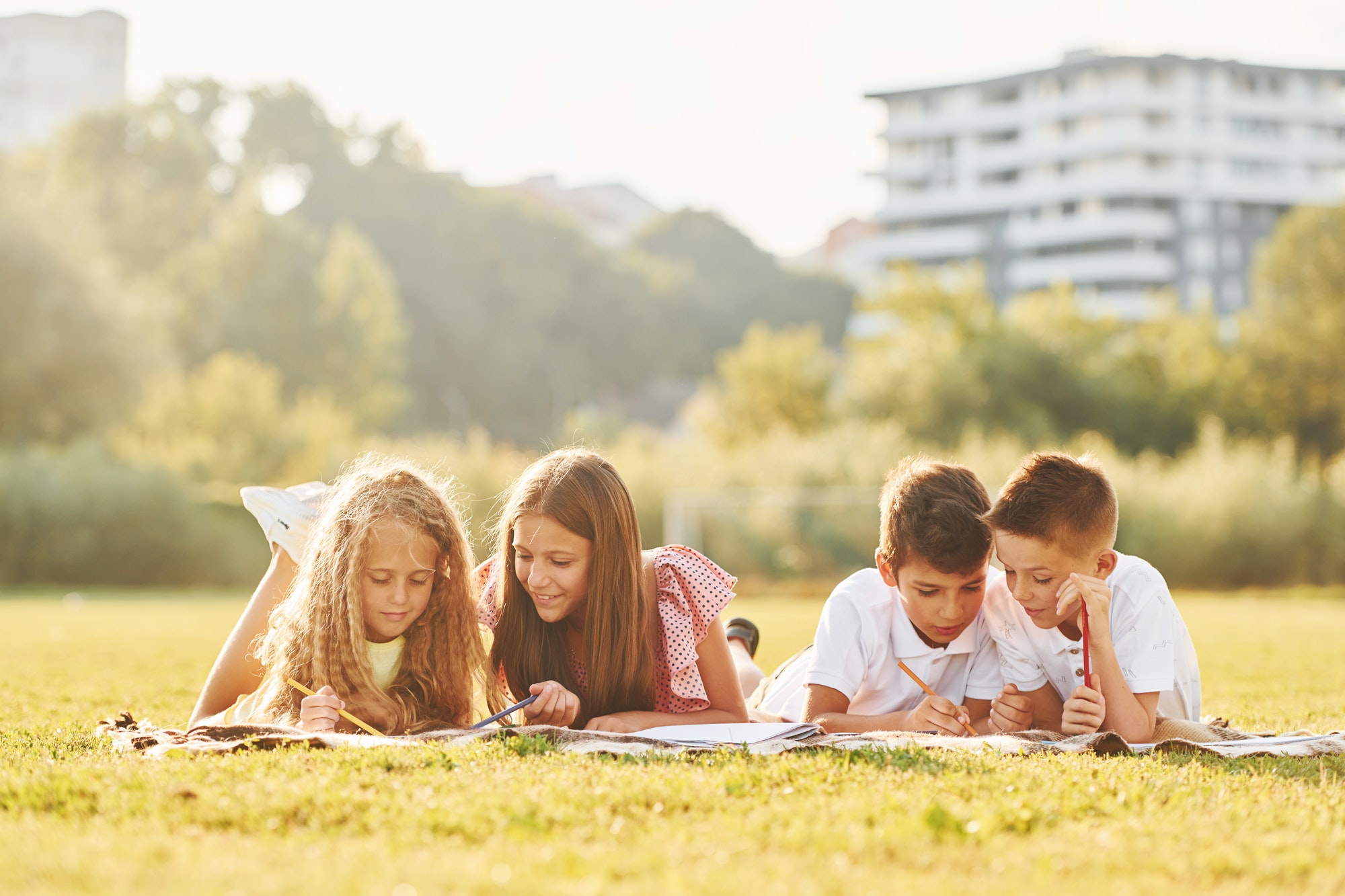 Laying down on the ground. Group of happy kids is outdoors on the sportive field at daytime