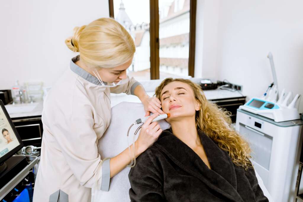 Professional young female doctor cosmetologist doing hydrafacial procedure in cosmetology clinic